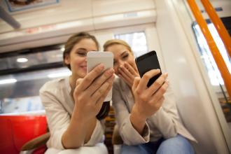 
		Two young women are in the subway looking at their smartphones
	